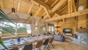 A spacious living area with a dining table set for six, a stone fireplace, and a television in the background.