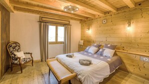 A wooden-paneled bedroom with a bed, a chair, a bench, and a window with curtains.