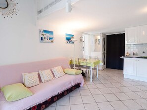 A living room with a pink sofa, a dining table with chairs, and a kitchen area with white cabinets.