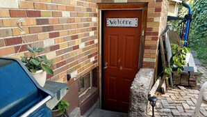 A brick building with a 'Welcome' sign, a barbecue grill, and a blue water pump. - Cozy Escape close to Yellowstone & Grand Teton NP, BYUI, River Beach sleeps 9 (St Anthony)