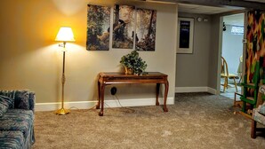 A carpeted room with a lamp, a wooden table with a plant, and three framed pictures on the wall. - Cozy Escape close to Yellowstone & Grand Teton NP, BYUI, River Beach sleeps 9 (St Anthony)