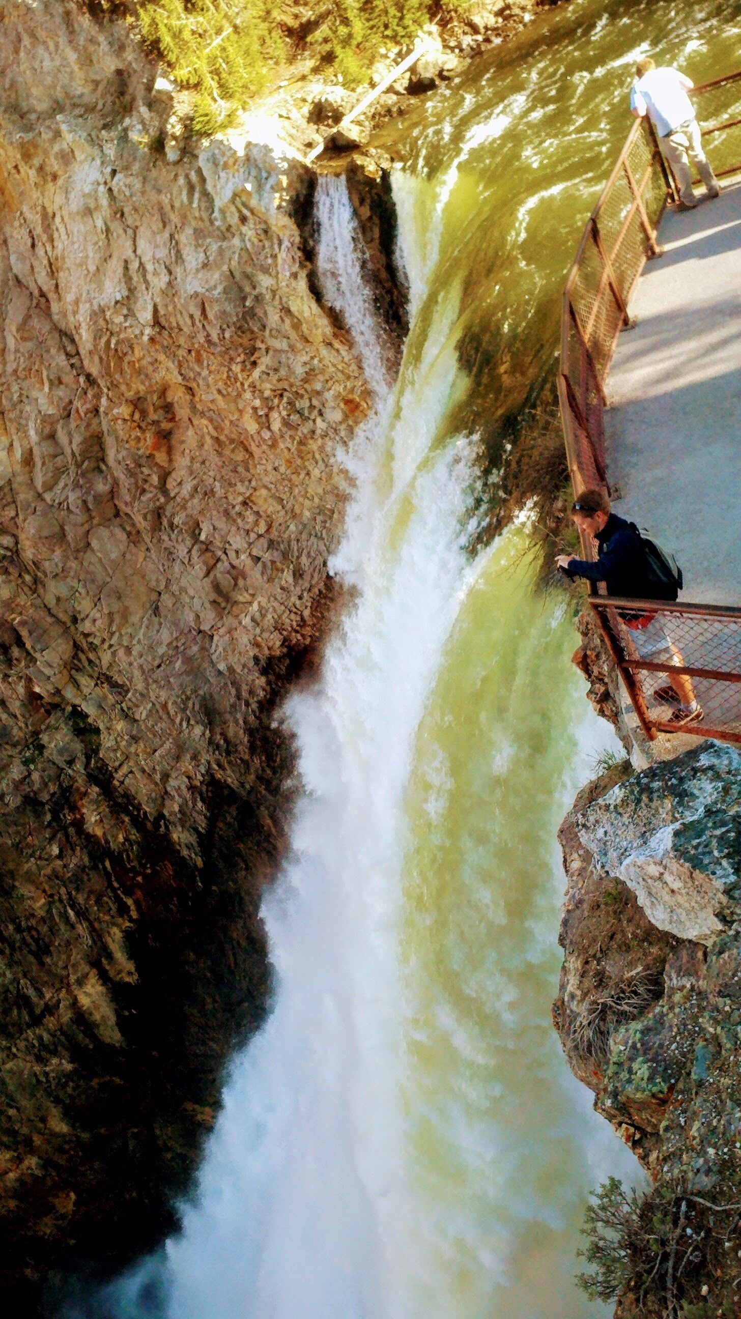 A waterfall cascading down a rocky cliff with a person standing on a bridge.