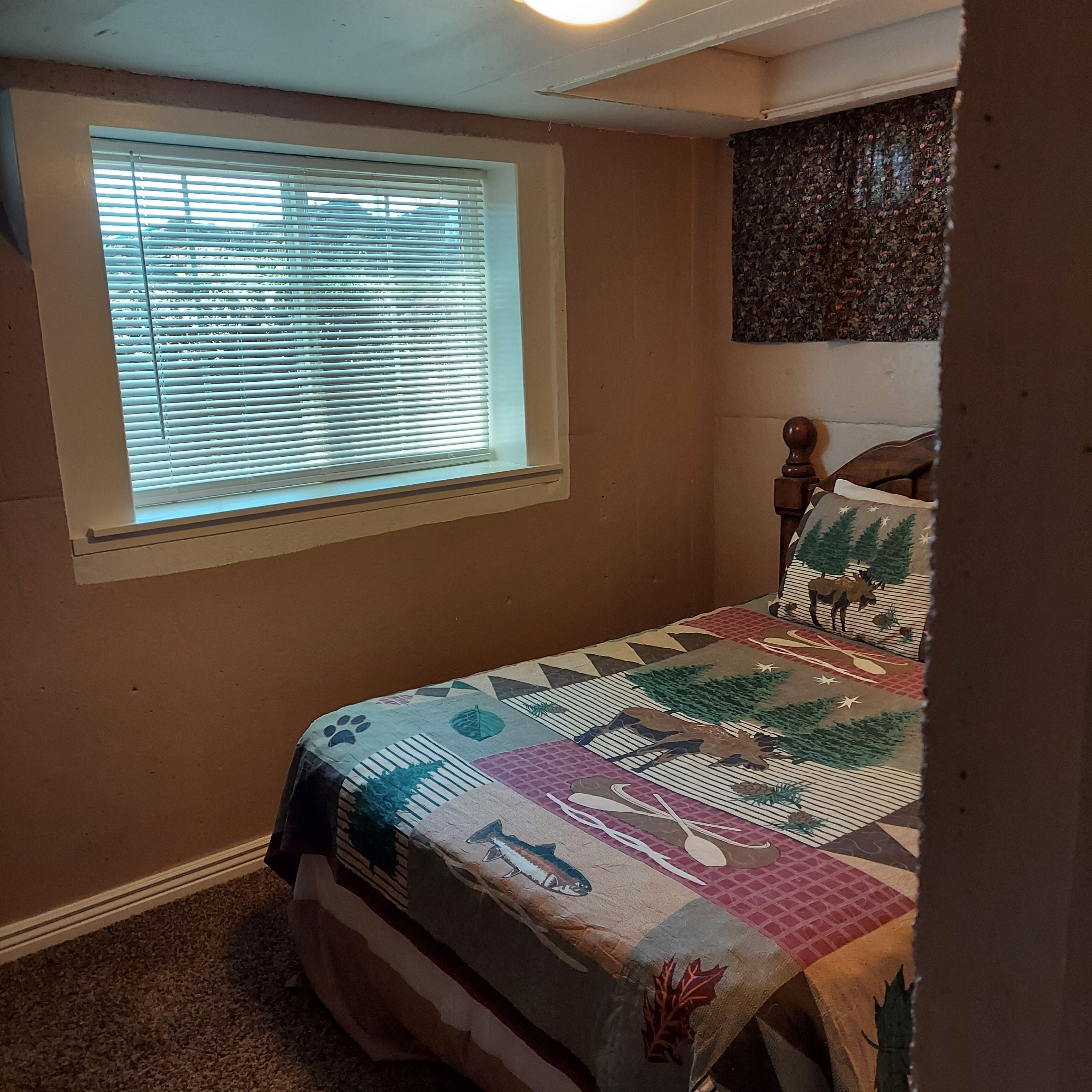Quarto com cama, janela com persianas, cabeceira e um objeto decorativo na parede.
