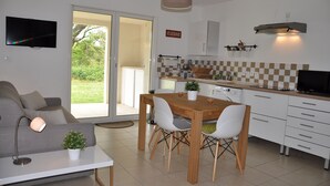 A modern kitchen with a dining table, chairs, and a TV mounted on the wall. - Charming apartment with large terrace and private pool 5 minutes from the beach (Santa-Lucia-Di-Moriani)