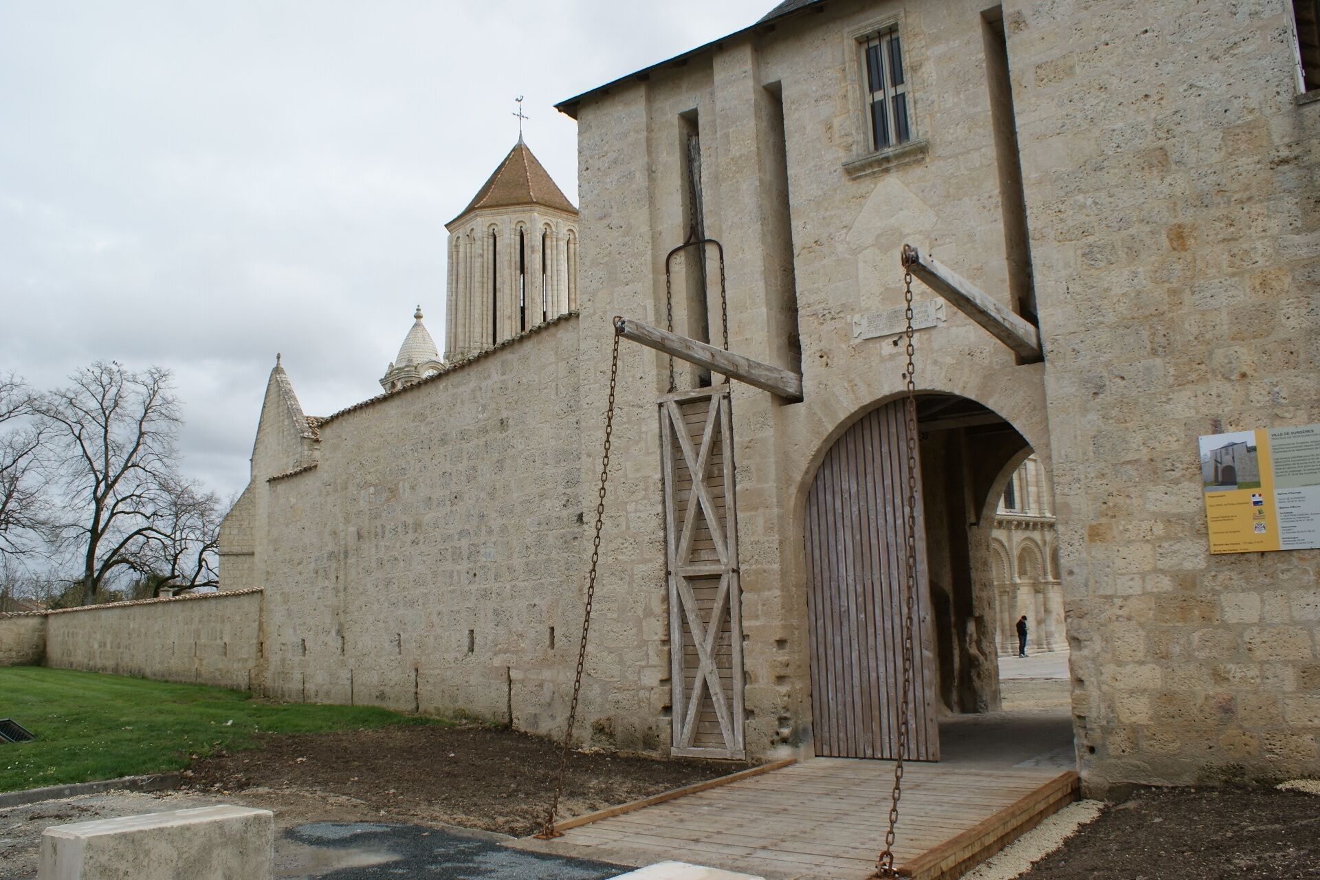 A historic stone building with a large wooden door, a metal gate, and a small tower.