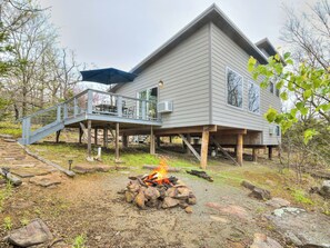 A two-story house with a deck, a fire pit, and a staircase leading to the deck.