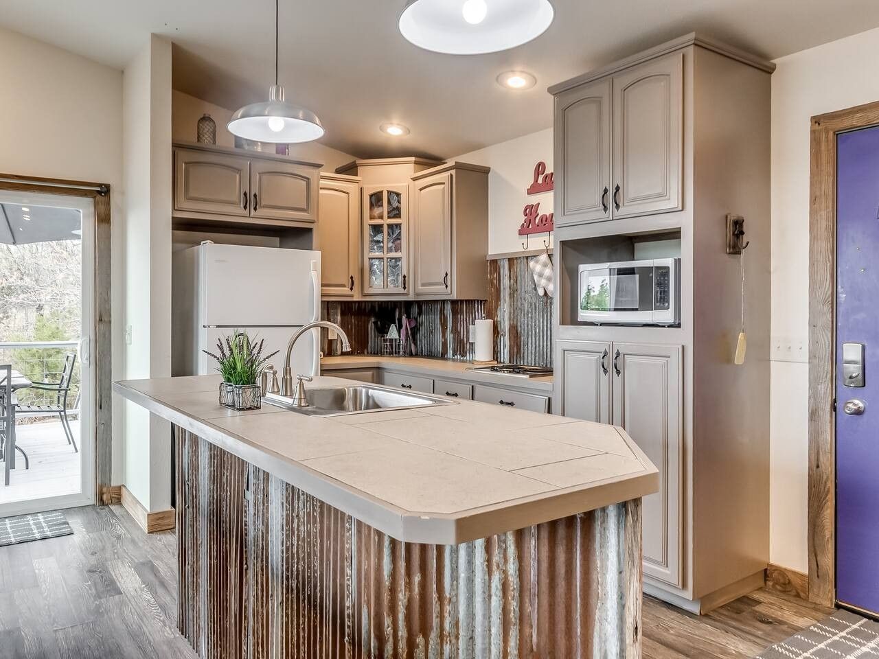 Una cocina con isla central, armarios, refrigerador y microondas.