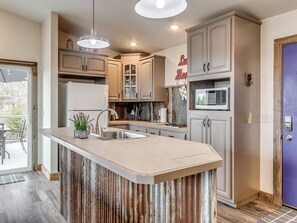 Una cocina con isla central, armarios, refrigerador y microondas.