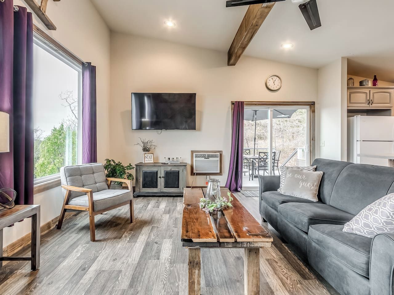 Un salon moderne avec un canapé gris, une table basse en bois et un téléviseur fixé au mur.