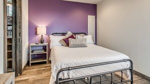 Une chambre à coucher avec un lit, une table de chevet, une lampe et un mur d’accent de couleur violette.
