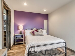 Un dormitorio con cama, mesita de noche, lámpara y una pared de acento morada.