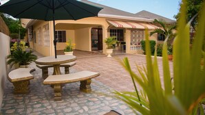 An outdoor patio area with a table and chairs, a green umbrella, and potted plants. - Beautiful Gated Community Vacation Home, Close to all Tourist Attractions (St. Anne's Bay)