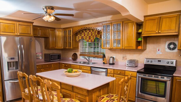 A kitchen with wooden cabinets, a stainless steel refrigerator, a microwave, a stove, and a dining area with wooden chairs and a table. - Beautiful Gated Community Vacation Home, Close to all Tourist Attractions (St. Anne's Bay)