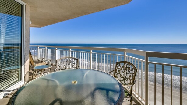 A balcony with a view of the ocean, a table, and two chairs. - Sophisticated Beach Chic Unit, Oceanfront Pool | Crescent Shores - S 1106 (North Myrtle Beach)