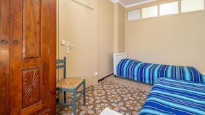 Een kamer met een houten garderobe, een stoel, een bed met gestreept beddengoed en vloertegels met een patroon.