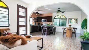 A spacious living area with a sofa, a coffee table, and a dining table with chairs. There is a kitchen in the background with a microwave and a refrigerator. - R Casa Unit 3 At Steps Beach (Rincon)