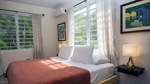 A hotel room with a bed, a nightstand, a lamp, and a window with curtains. - R Casa Unit 3 At Steps Beach (Rincon)