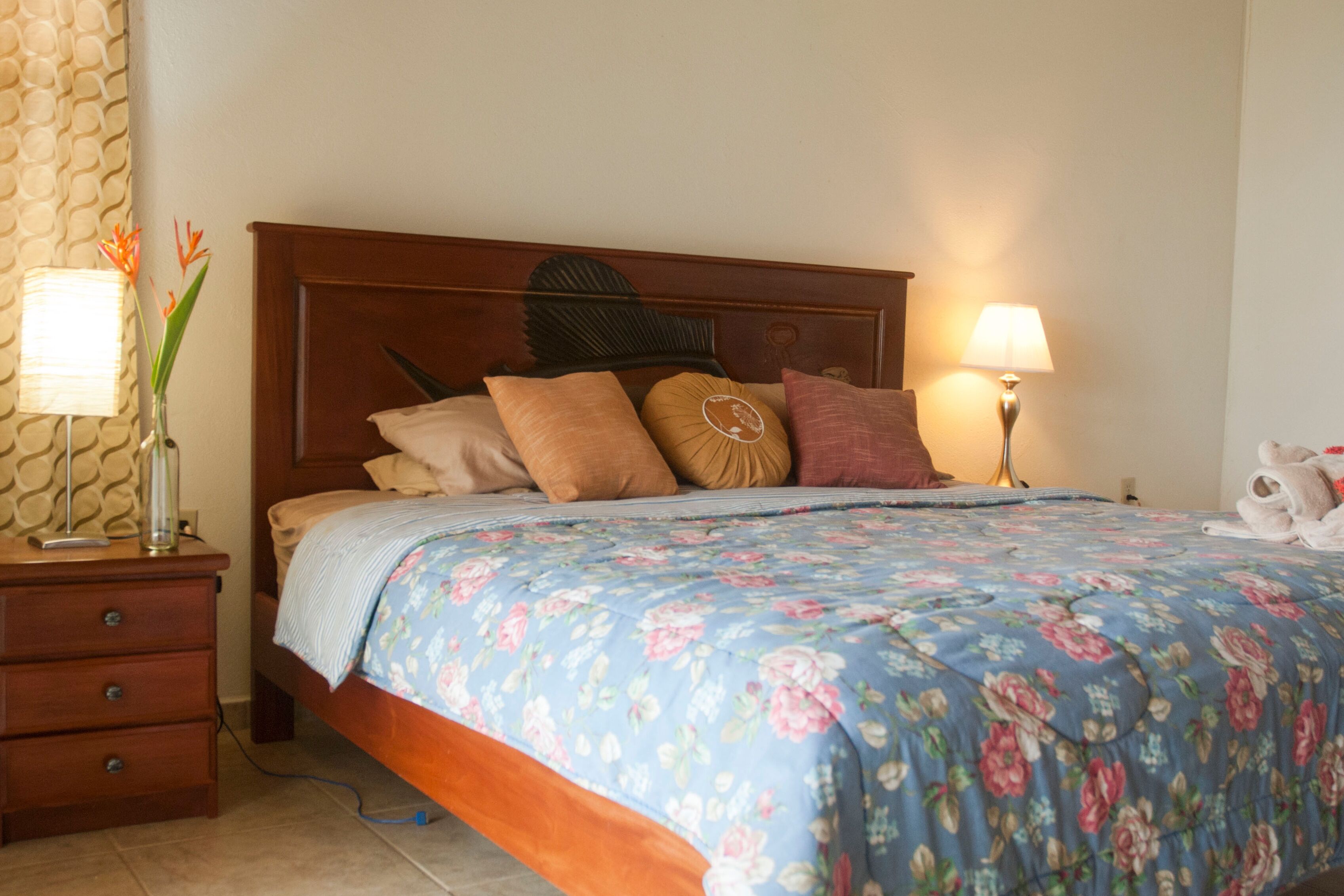 Un lit bien fait, avec une couvre-lit à motifs floraux, une tête de lit en bois et une lampe de chevet.