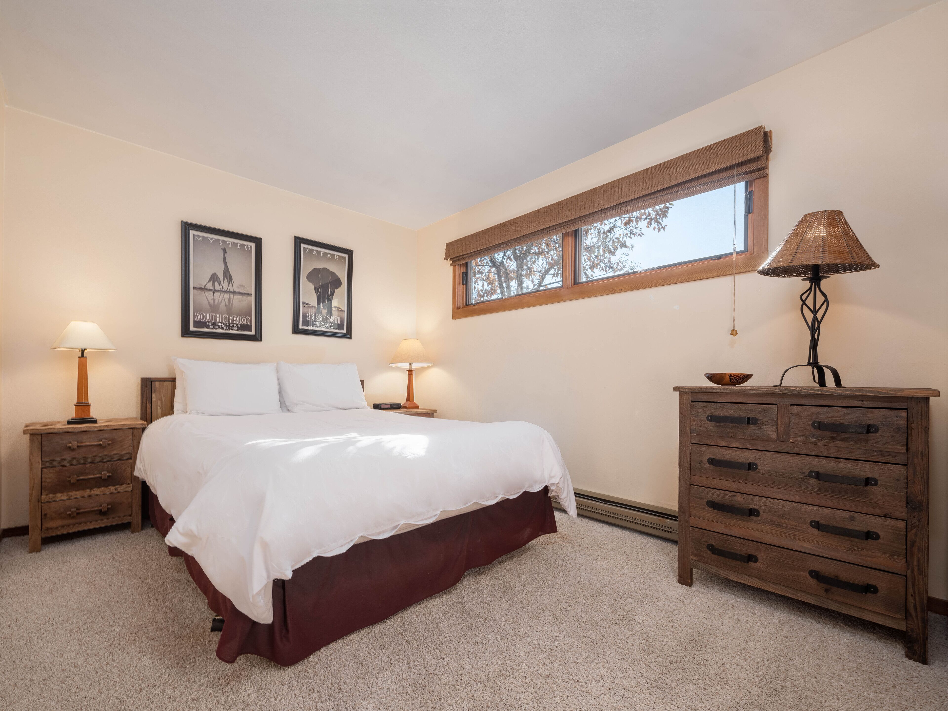 A bedroom with a bed, two bedside tables, a dresser, and two wall-mounted lamps.