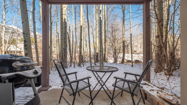A covered patio with a grill and two chairs, surrounded by trees and snow. - RMR: Sagebrush 1311 Condo in The Aspens/Wilson,WY (Wilson)