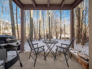 A covered patio with a grill and two chairs, surrounded by trees and snow. - RMR: Sagebrush 1311 Condo in The Aspens/Wilson,WY (Wilson)