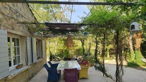 Eine Terrass mit Tisch und Stühlen, umgeben von Pflanzen und einem Pergola.