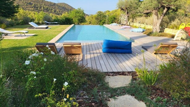 Ein rechteckiger Pool mit Holzterrasse und Liegestühlen.