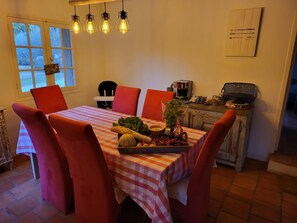 Un coin repas avec une table dressée pour quatre personnes, des chaises rouges, une nappe à carreaux et une variété de fruits et de légumes disposés sur la table.