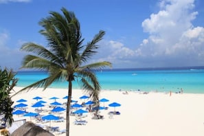 A beach with white sand, clear turquoise water, and palm trees.