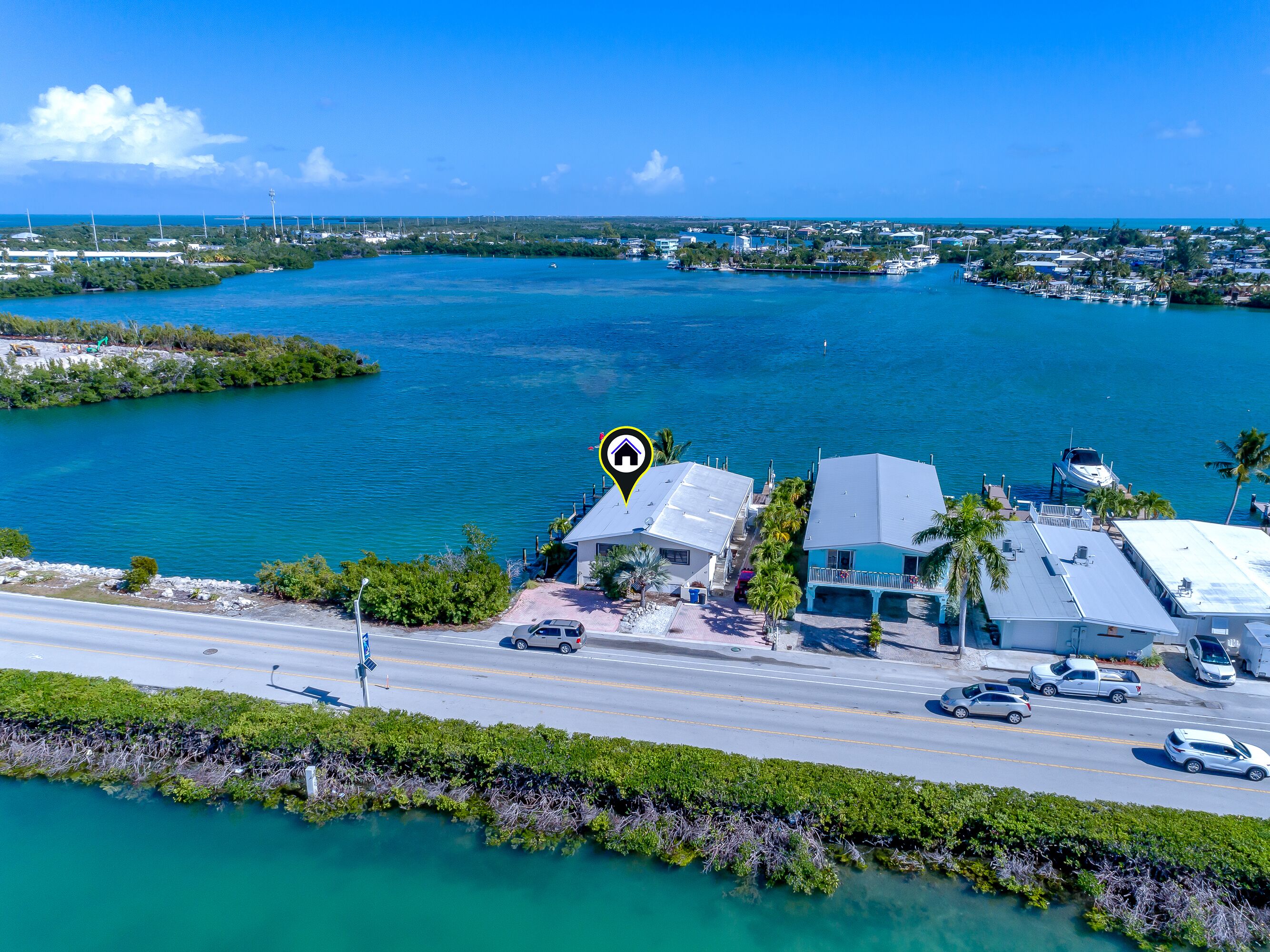 A coastal property with a road leading to a house, a boat dock, and a marina in the background.