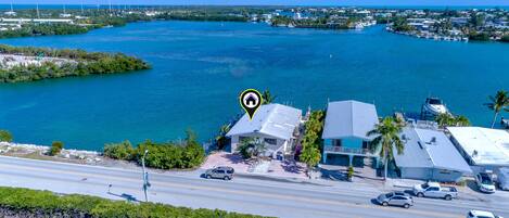 A coastal property with a road leading to a house, a boat dock, and a marina in the background.