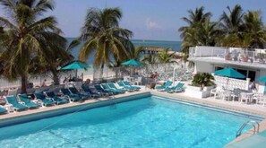 A pool area with lounge chairs and umbrellas, a view of the ocean, and a building with a balcony. - Waterfront W/270 degree views, Cabana Club, Multiple Docks (Key Colony Beach)