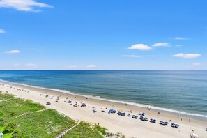 Een strand met rijen parasols en ligbedden, een heldere lucht en een rustige zee.