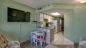 A compact kitchen with a microwave, stove, and refrigerator. There is a small dining area with a table and chairs. - Tropical 3rd Floor Unit, Indoor and Outdoor Amenities | Sea Watch S - 311 (Myrtle Beach)