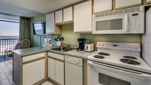 A compact kitchen with a microwave, stove, and sink. A chair and a small table are visible near the window. - Tropical 3rd Floor Unit, Indoor and Outdoor Amenities | Sea Watch S - 311 (Myrtle Beach)