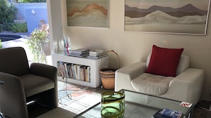 A living room with a glass coffee table, a white sofa with a red pillow, a bookshelf, and two paintings on the wall. - Location, location, location!  El Paseo Jewel in the desert  (Palm Desert)