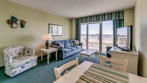Une chambre d’hôtel avec un canapé, un fauteuil, une petite table, une télévision et un balcon avec vue.