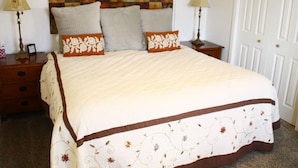 Un lit bien fait, avec une couvre-lit à motifs floraux et des oreillers, une tête de lit décorative, des lampes de chevet et une porte fermée, dans une chambre à coucher.