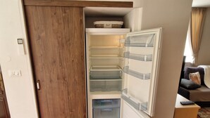 Un espace de vie compact doté d’un réfrigérateur int égré, d’une porte en bois et d’un petit coin salon avec un canapé et une table d’appoint.