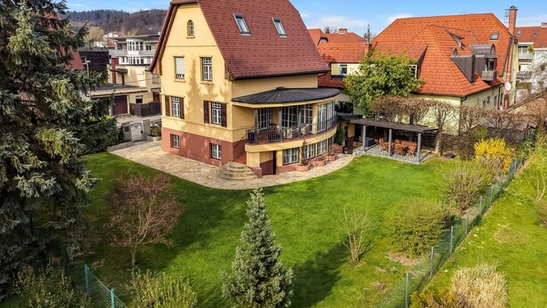 Une maison à deux étages dotée d’un balcon incurvé, d’une pelouse bien entretenue et d’une clôture qui l’entoure.