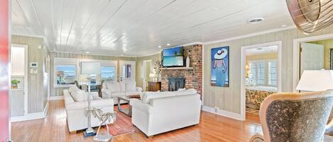 A spacious living room with a fireplace, white furniture, and a large TV.