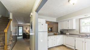 Cocina con alacenas blancas, un refrigerador y un lavavajillas. Hay una ventana que proporciona luz natural y una puerta que da a otra habitación.
