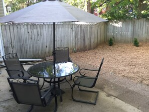 Une table ronde en verre, quatre chaises, un parasol et une clôture en bois en arrière-plan.
