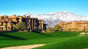 Un campo da golf con montagne sullo sfondo, che include una club house con diversi edifici e un verde curato.