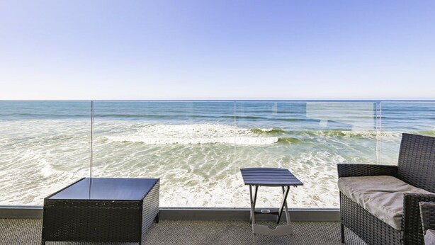 Un balcon avec vue sur l’océan, une petite table et deux chaises en osier.