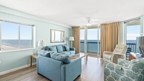 Een woonkamer met een bank, fauteuils, een salontafel, een televisie en een balkon met uitzicht op de oceaan.