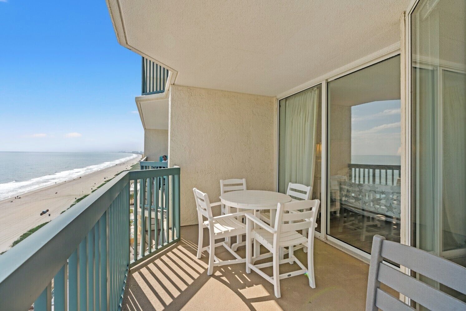 A balcony with a table and chairs, overlooking a beach.