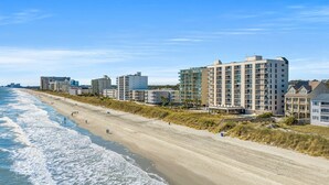 Et hotel ved stranden med flere etager, en sandstrand og bølger.
