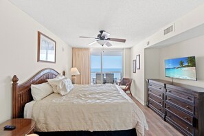 Ein Hotelzimmer mit Bett, Deckenventilator, Fernseher, Kommode und einem Balkon mit Meerblick.