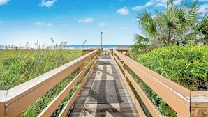 Ein hölzerner Steg führt zu einem Strand unter blauem Himmel.